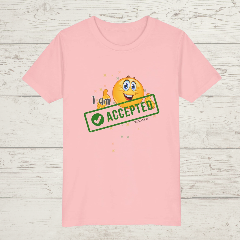 Pink t-shirt with a emoji character and 'I am accepted' text on a wooden surface