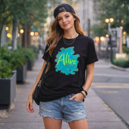 Woman wearing a black t-shirt with a colorful 'Alive' graphic and text, standing on a city street.