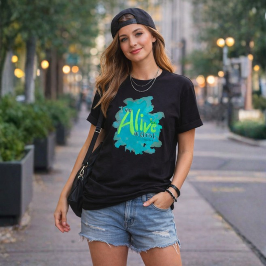 Woman wearing a black t-shirt with a colorful 'Alive' graphic and text, standing on a city street.