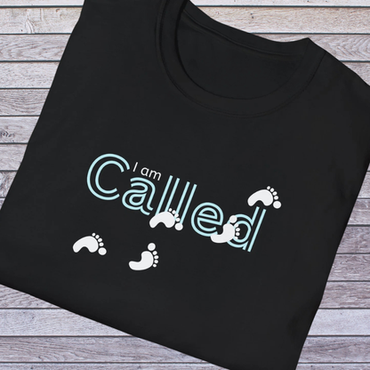 Black t-shirt with 'I am Called' text and footprints on a wooden surface