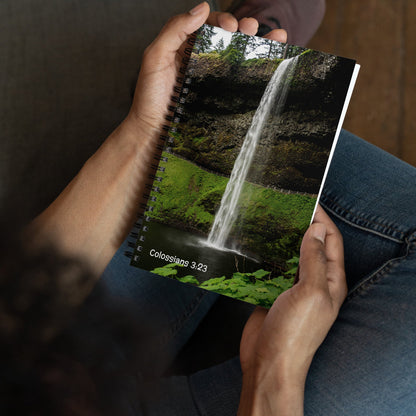 Person holding a notebook with a waterfall design and text on the cover.