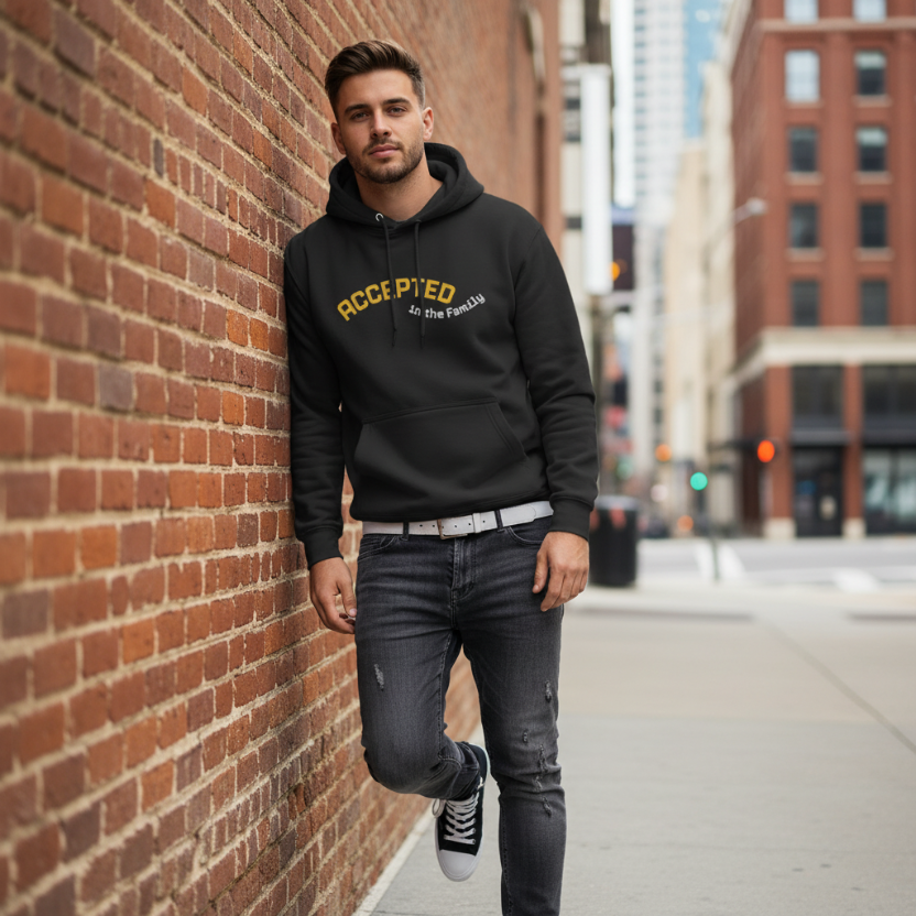 Black hoodie with text 'ACCEPTED in the Family' on a brick wall background, with sneakers and jeans on top.