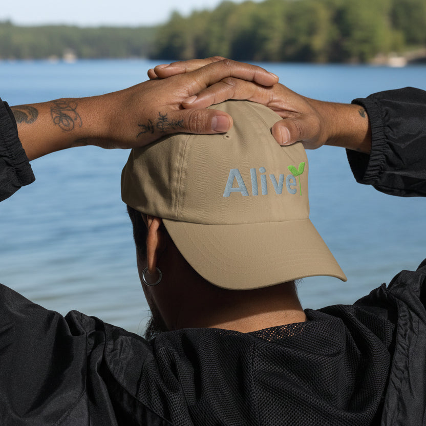 Person wearing a beige cap with 'Alive' logo, hands clasped together