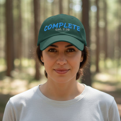 Dark green cap with blue 'COMPLETE Gal. 2:20' girl outside in trees
