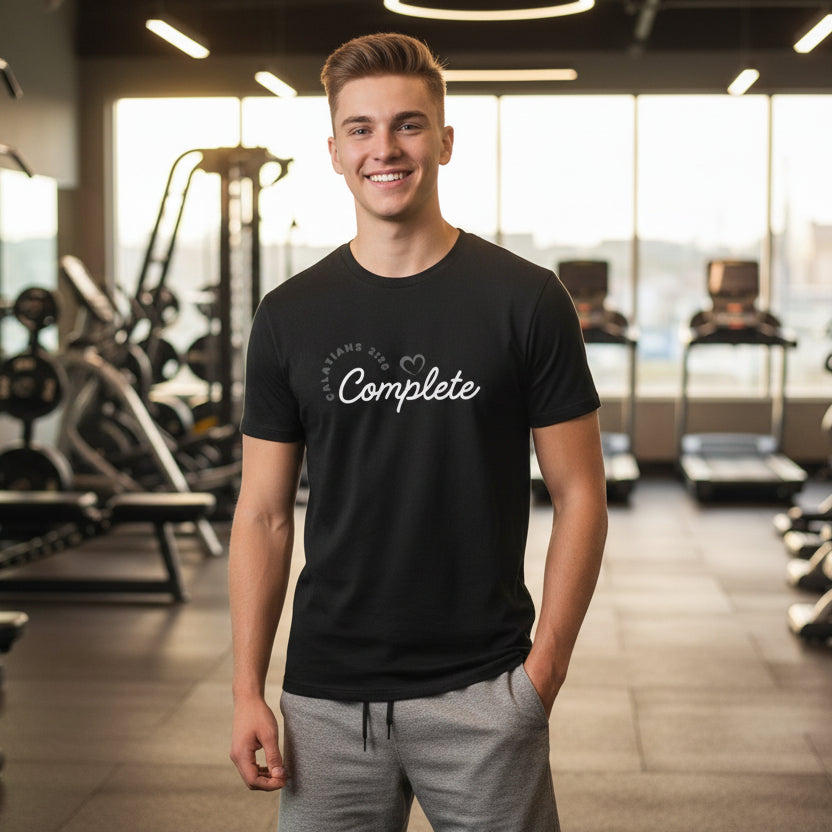 Black t-shirt with text 'Complete, Galatians 2:20' and a heart, worn by a guy standing in the weight room