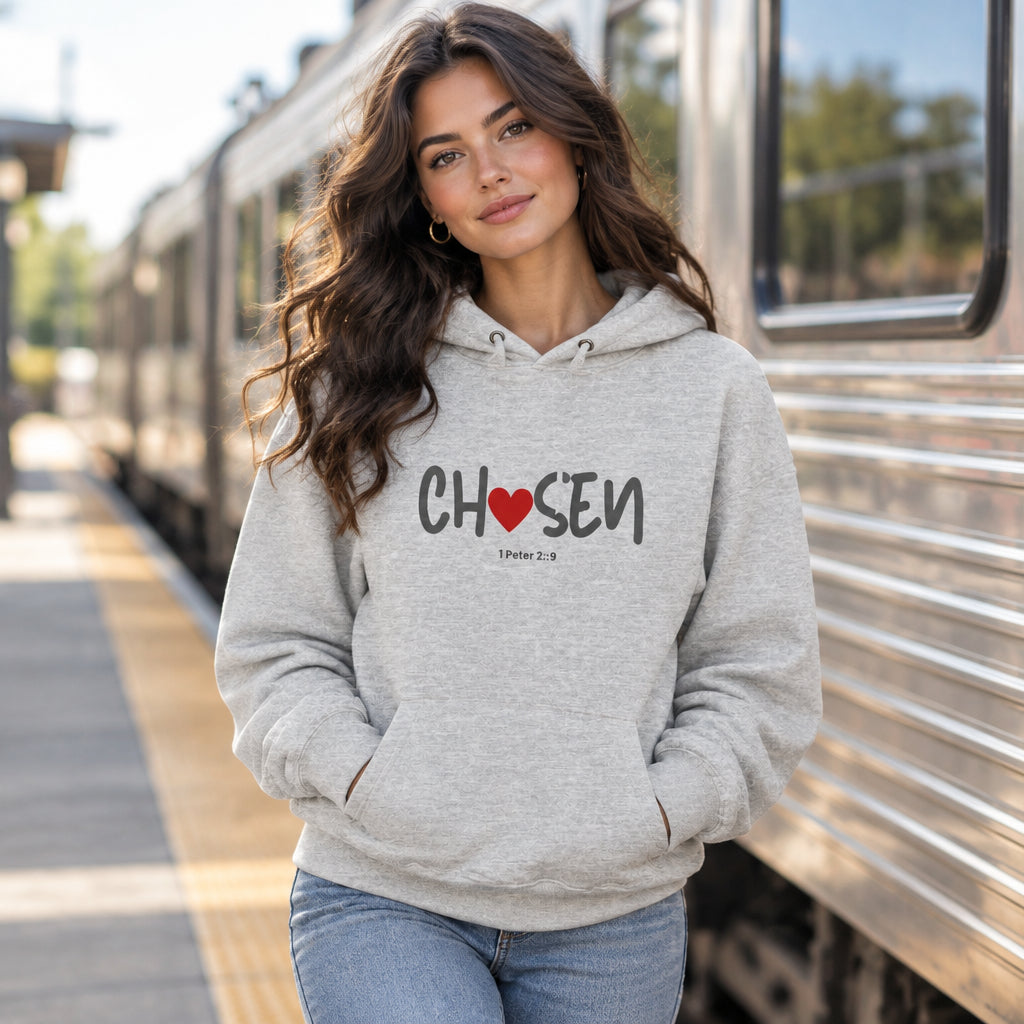 A light gray heather pullover hoodie worn by a female model outside near a train. The hoodie features the word 'CHOSEN' printed across the chest in dark gray, with a red heart symbol replacing the letter 'O', and the Bible verse '1 Peter 2:9' printed below.