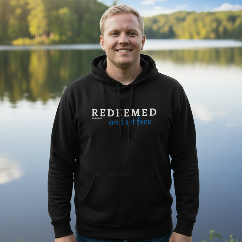 Black hoodie with 'REDEEMED and set free' text outside on a sunny day by the lake