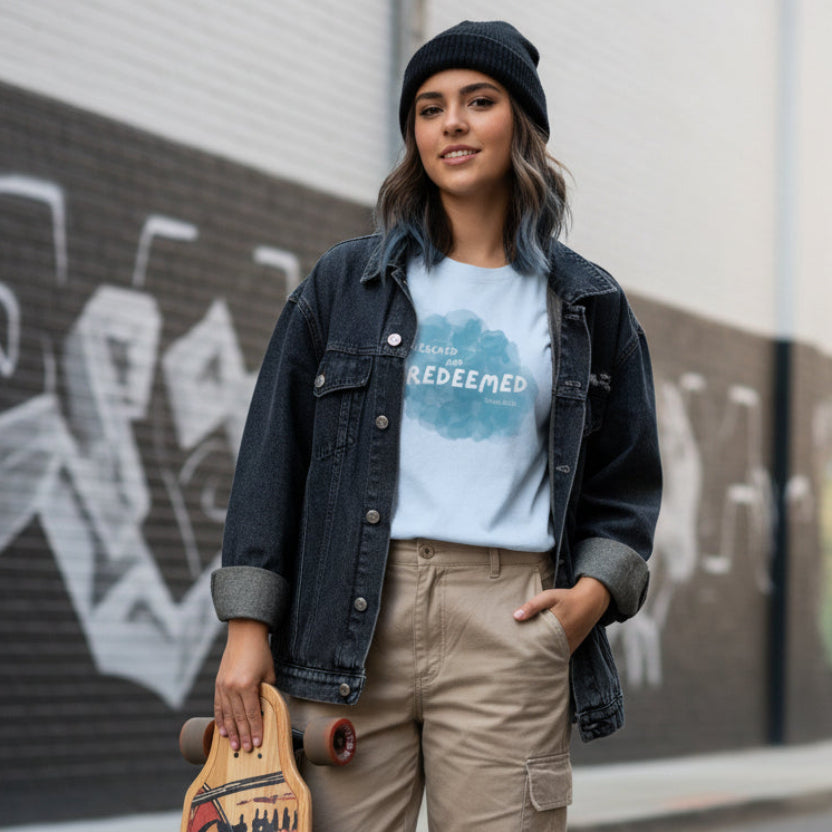 Light blue t-shirt with a 'Rescued and Redeemed' graphic, worn by streetwear female with longboard