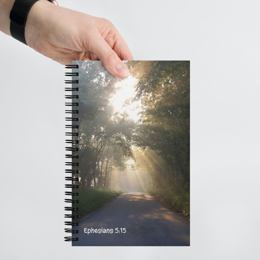 Notebook with a scenic cover of a sunlit path and trees, held by a hand.