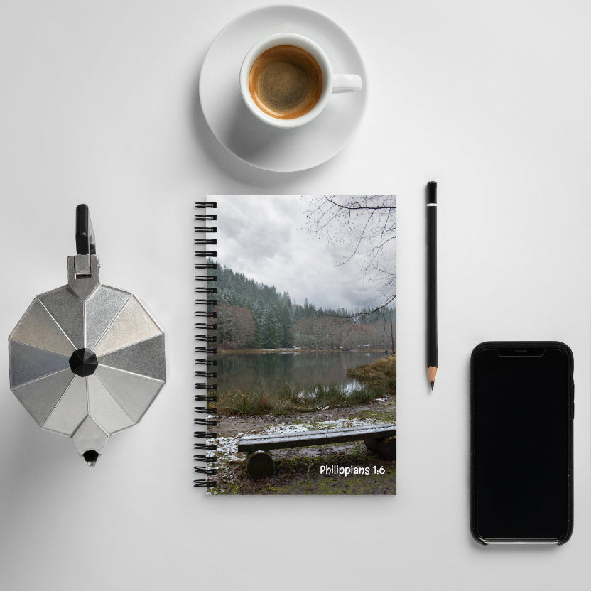 Notebook with a nature scene cover, coffee cup, pen, and phone on a light gray background
