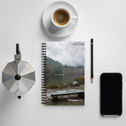 Notebook with a nature scene cover, coffee cup, pen, and phone on a light gray background