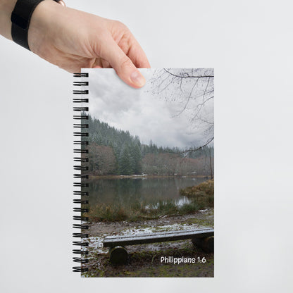 Notebook with a scenic cover featuring a lake and trees, held by a hand.