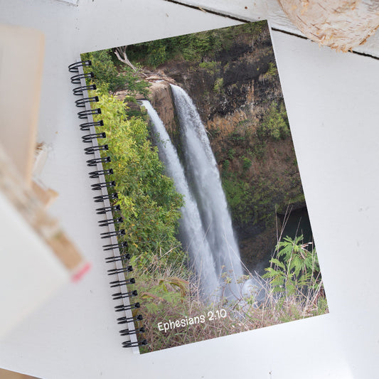 Notebook with a waterfall design and 'Ephesians 2:10' text on a white surface.
