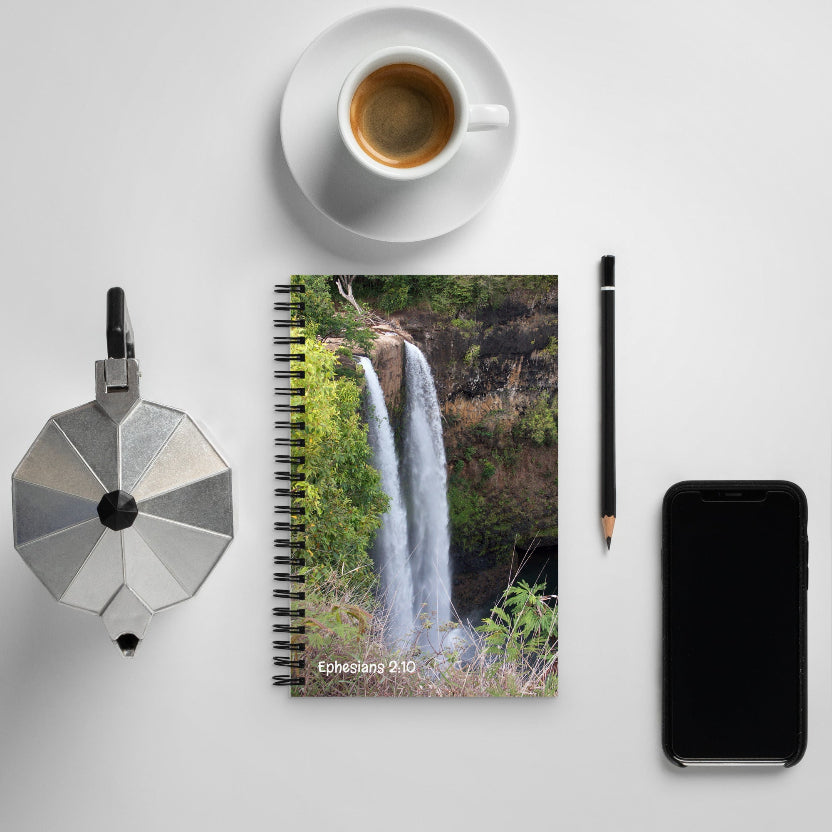 Notebook with waterfall design, coffee cup, pen, and phone on a light gray surface