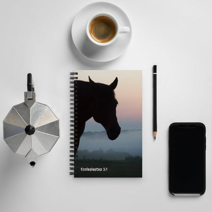 Notebook with horse silhouette cover, coffee cup, phone, and other items on a light surface