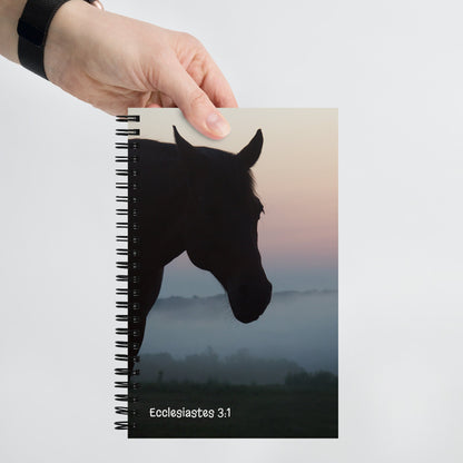 Notebook with a horse silhouette cover and 'Ecclesiastes 3:1' text, held by a hand.