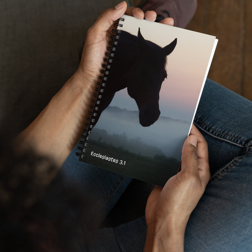 Person holding a notebook with a horse illustration on a blurred landscape background
