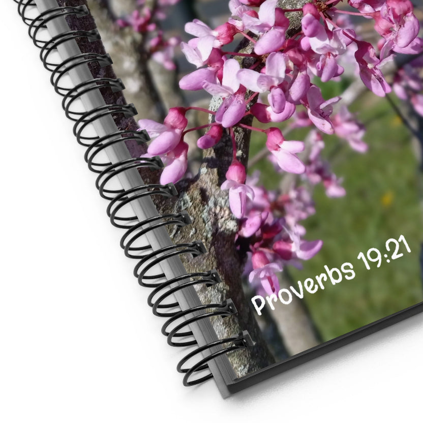 Spiral-bound notebook with pink flowers and 'Proverbs 19:21' text on a white background