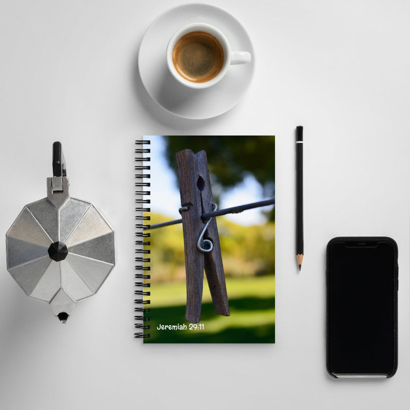 Notebook with a wooden clothespin on a grassy background, surrounded by a coffee cup, pencil, and phone on a light surface.