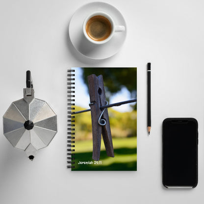 Notebook with a wooden clothespin on a grassy background, surrounded by a coffee cup, pencil, and phone on a light surface.