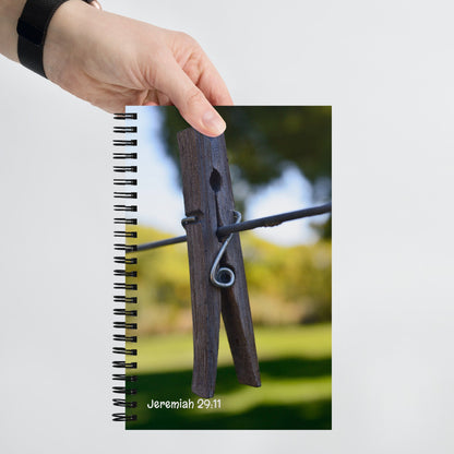 Notebook with a wooden clothespin design on the cover, held by a hand against a blurred outdoor background.
