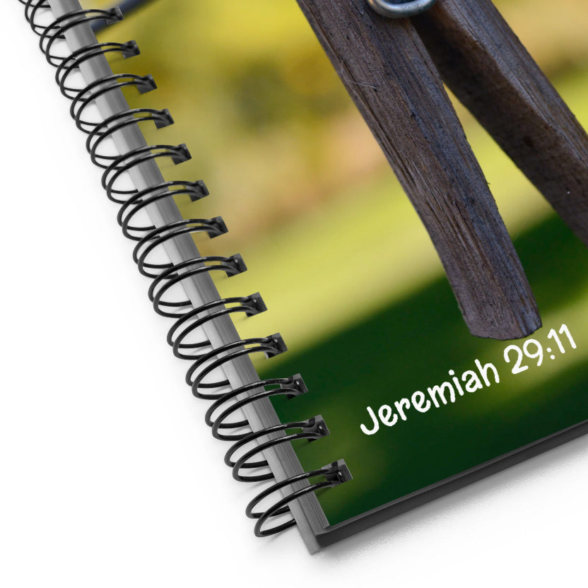 Notebook with spiral binding and wooden clip on a blurred green background with 'Jeremiah 29:11' text.