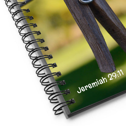 Notebook with spiral binding and wooden clip on a blurred green background with 'Jeremiah 29:11' text.