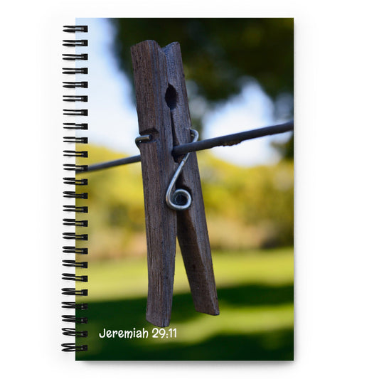Notebook with a wooden clothespin on a wire against a blurred outdoor background in New Mexico, featuring the text 'Jeremiah 29:11'.