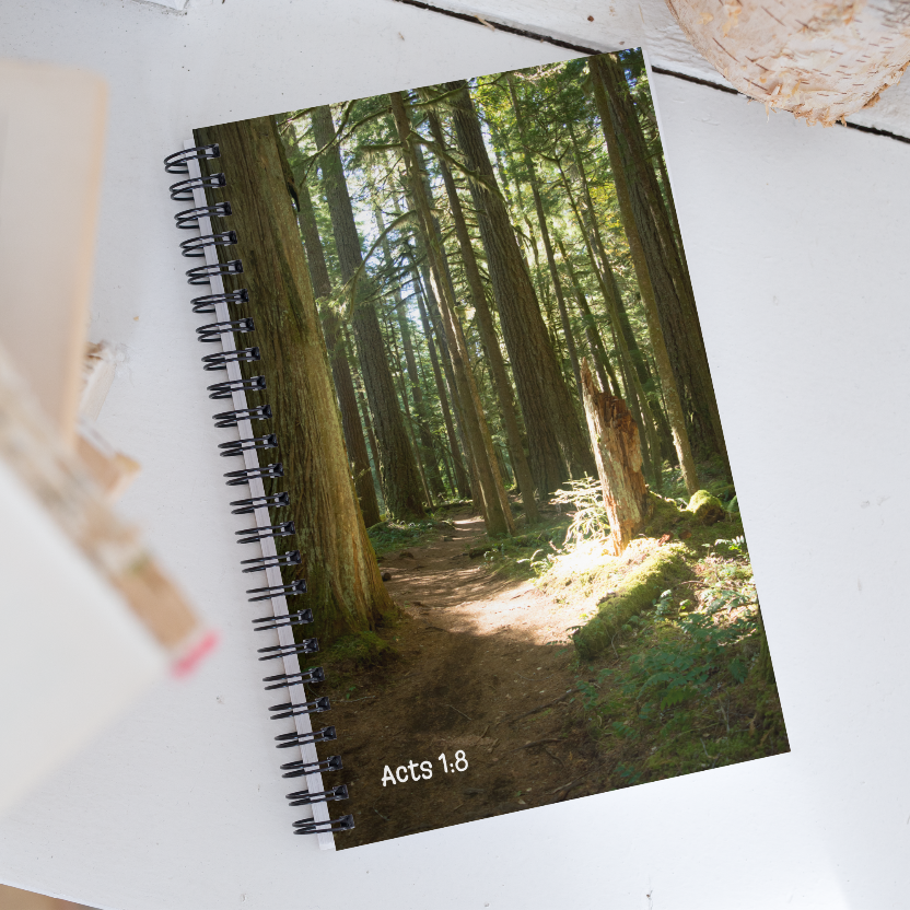 Notebook with a forest cover and 'Acts 1:8' text on a white surface