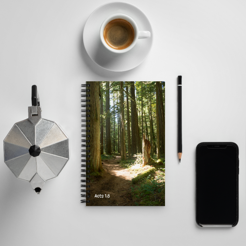 Notebook with a forest design, coffee cup, pen, and phone on a white surface