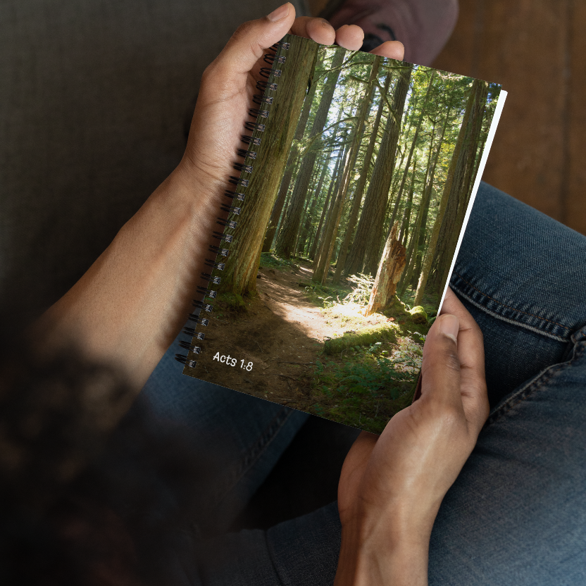 Person holding a notebook with a forest cover, sitting on a wooden floor.