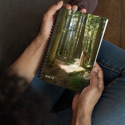 Person holding a notebook with a forest cover, sitting on a wooden floor.