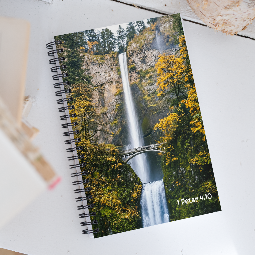 Notebook with a waterfall design and '1 Peter 4:10' text on a white surface