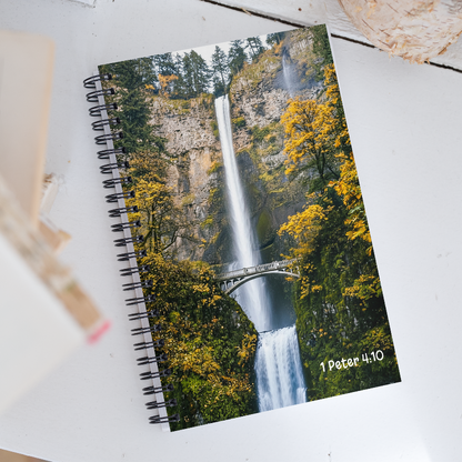 Notebook with a waterfall design and '1 Peter 4:10' text on a white surface