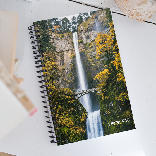 Notebook with a waterfall design and '1 Peter 4:10' text on a white surface