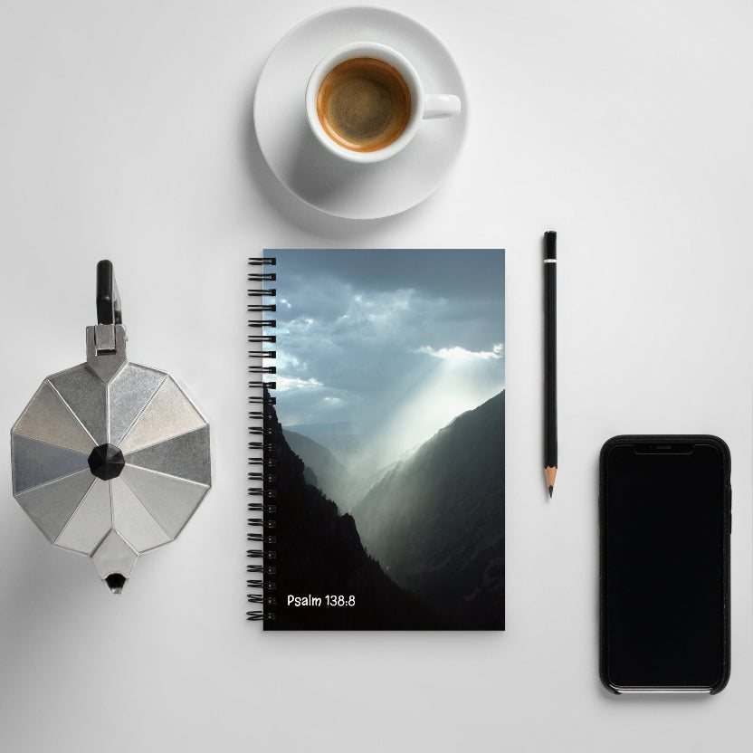 Notebook with mountain design, coffee cup, pen, and phone on a white surface