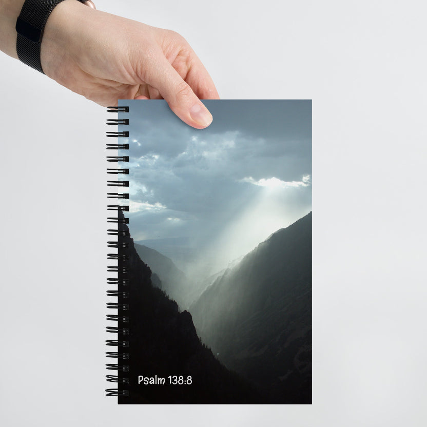 Notebook with mountain design and 'Psalm 138.8' text held by a hand on a white background