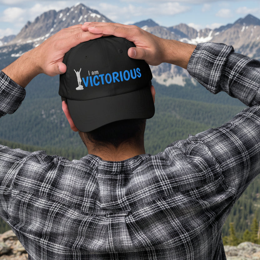 Person wearing a navy blue cap with 'Accepted' text, holding it while looking at a mountain scene